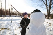 Молодая девушка смеется над снеговиком, делая лицо — стоковое фото