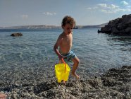 Kleiner Junge trägt eine leuchtend gelbe Wasserfahne in Meeresnähe — Stockfoto