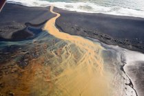 Luftaufnahme des geflochtenen orangen Flusses, der in Südisland in den Ozean fließt — Stockfoto