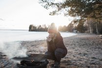 Woman warming up by a fire at the beach in winter in Sweden — Stock Photo