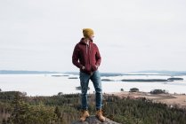 Man standing on a rock whilst hiking a hill above the ocean in Sweden — Stock Photo
