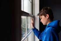 Tween menino olhando para fora de uma janela em um quarto escuro. — Fotografia de Stock