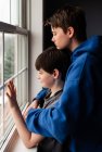 Deux garçons regardant par la fenêtre avec des visages tristes — Photo de stock