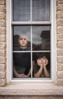 Deux garçons regardant par la fenêtre avec des visages ennuyés — Photo de stock