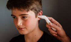 Мальчик-подросток получает температуру с помощью ушного термометра. — стоковое фото