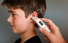 Tween niño consiguiendo temperatura tomada con un termómetro del oído. - foto de stock