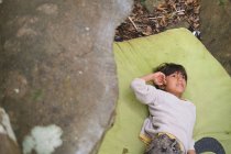 Menino descansa em um crashpad ao lado de uma rocha — Fotografia de Stock