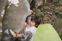 Un ragazzino si arrampica su una roccia all'aperto — Foto stock