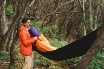Чоловік упаковує спальний мішок і гамак на кемпінгу в лісі — стокове фото