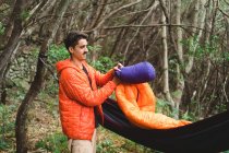 Мужчина собирает спальный мешок и гамак в кемпинге в лесу — стоковое фото