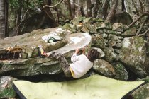 Un niño trepa una roca en un bosque - foto de stock