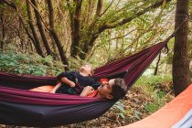 A man and a young kid lying in a hammock in the forest — Stock Photo