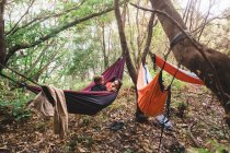 Un homme et un jeune enfant couchés dans un hamac dans la forêt — Photo de stock