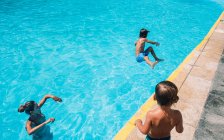A woman and kid look at a boy jumping into a pool — Stock Photo
