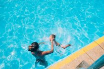 Женщина помогает своему ребенку прыгнуть в бассейн — стоковое фото