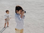 Kind macht Foto mit Oldtimer-Kamera, während anderes Kind im Hintergrund steht — Stockfoto