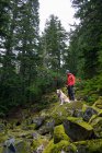 Homme randonneur et chien moelleux debout sur des rochers mousseux dans les montagnes — Photo de stock