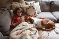 Красивая девушка со смартфоном расслабляется в постели со своей собакой — стоковое фото