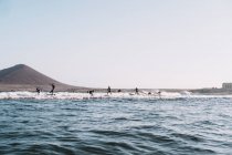 Pulled back view of surfers riding a small wave at sunset — Stock Photo