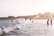 Тянул назад вид серферов и людей на пляже на закате — стоковое фото