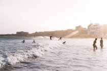 Vue arrière des surfeurs et des personnes sur la plage au coucher du soleil — Photo de stock