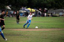 Юный футболист капает мяч во время игры — стоковое фото