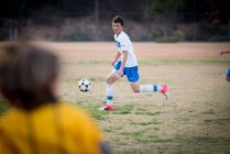 Adolescente futbolista dribleando la pelota durante un juego - foto de stock