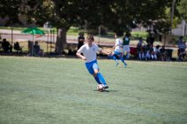 Adolescente jogador de futebol driblando a bola durante um jogo — Fotografia de Stock