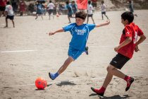 Young soccer player player flying trough the air about to kick the ball during a beach soccer game — Stock Photo