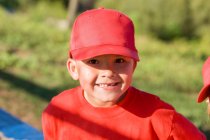 Молодий хлопець втратив зуб у червоній бейсбольній шапці, посміхаючись на камеру — стокове фото