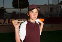 Retrato de un jugador de béisbol de secundaria con uniforme granate sosteniendo su bate - foto de stock