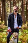 Retrato de jovem homem tatuado com seu cão na floresta — Fotografia de Stock