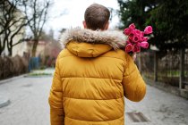 Blond man in a yellow winter jacket with a bouquet of tulips in hands — Stock Photo