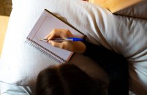 Mujer acostada en la cama escribiendo en su agenda. - foto de stock