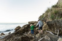 Père et fils se tenant la main marchant sur des rochers près de l'océan — Photo de stock
