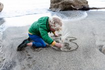 Kleines Kind schreibt Ich liebe Mama im Sand an einem Strand in Neuseeland — Stockfoto