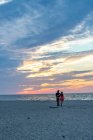 Молода пара йде в бік океану на барвистому заході сонця — стокове фото