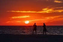 Молода пара ходить уздовж пляжу на заході сонця — стокове фото