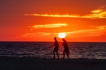 Giovane coppia a piedi lungo la spiaggia al tramonto — Foto stock