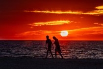 Молода пара ходить уздовж пляжу на заході сонця — стокове фото