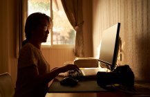 Une femme travaillant sur un ordinateur dans une pièce remplie de lumière chaude du matin — Photo de stock