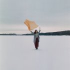 A woman stands on the shore of a frozen lake in a yellow scarf — Stock Photo