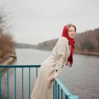 Une femme se tient sur le bord de la rivière dans une écharpe rouge — Photo de stock
