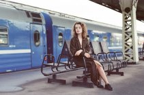 Une femme assise près d'un train dans une gare — Photo de stock