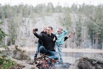 Father taking selfies with his kids whilst sitting next to a campfire — Stock Photo