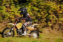12 year old boy riding his motocross motorcycle through field — Stock Photo