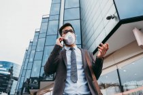 Homem de negócios com máscara protetora usando telefone na rua da cidade — Fotografia de Stock
