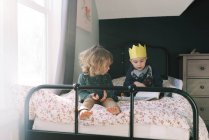 Hermanos jugando juntos en la cama y leyendo libros. - foto de stock