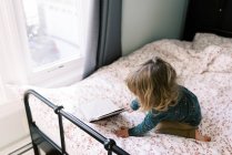 Bambina che gioca sul suo letto e legge un libro. — Foto stock