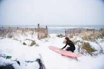 Donna con tavola da surf sulla spiaggia in inverno, New England. — Foto stock